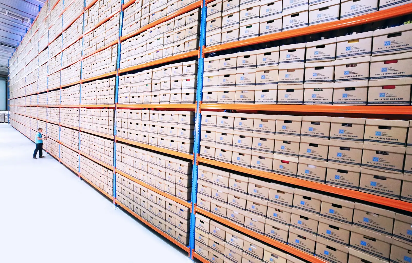 Hohe Regalwand mit beschrifteten Archivkartons in einer großen Halle, Symbolbild